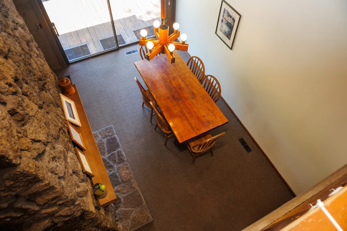 This image shows a long wooden dining table beneath a unique chandelier, with a stone wall adding rustic charm to the background. The space is clearly designed for communal meals and gatherings, offering a warm and welcoming atmosphere ideal for groups.