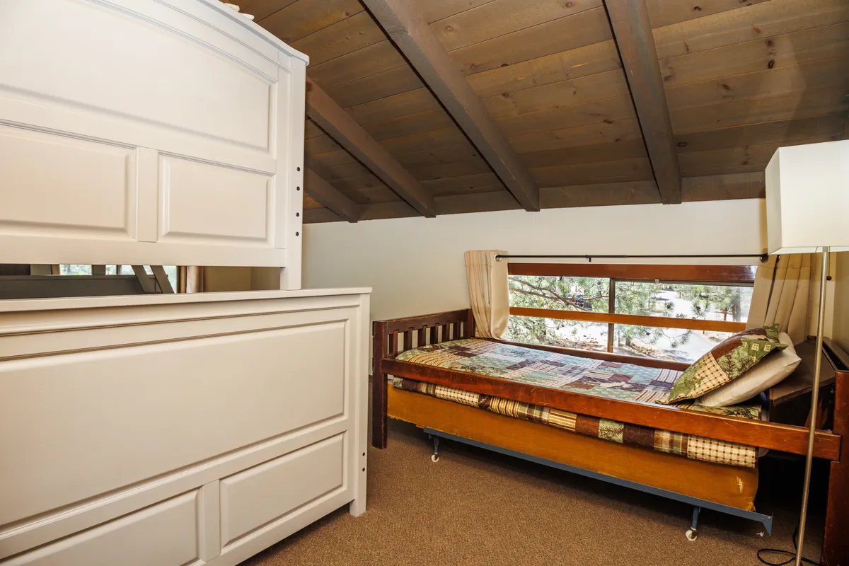 This image features a serene bedroom with a wooden bed, a matching dresser, and a large window that lets in ample natural light. The room exudes a calm, inviting atmosphere, perfect for rest and relaxation after a busy day.