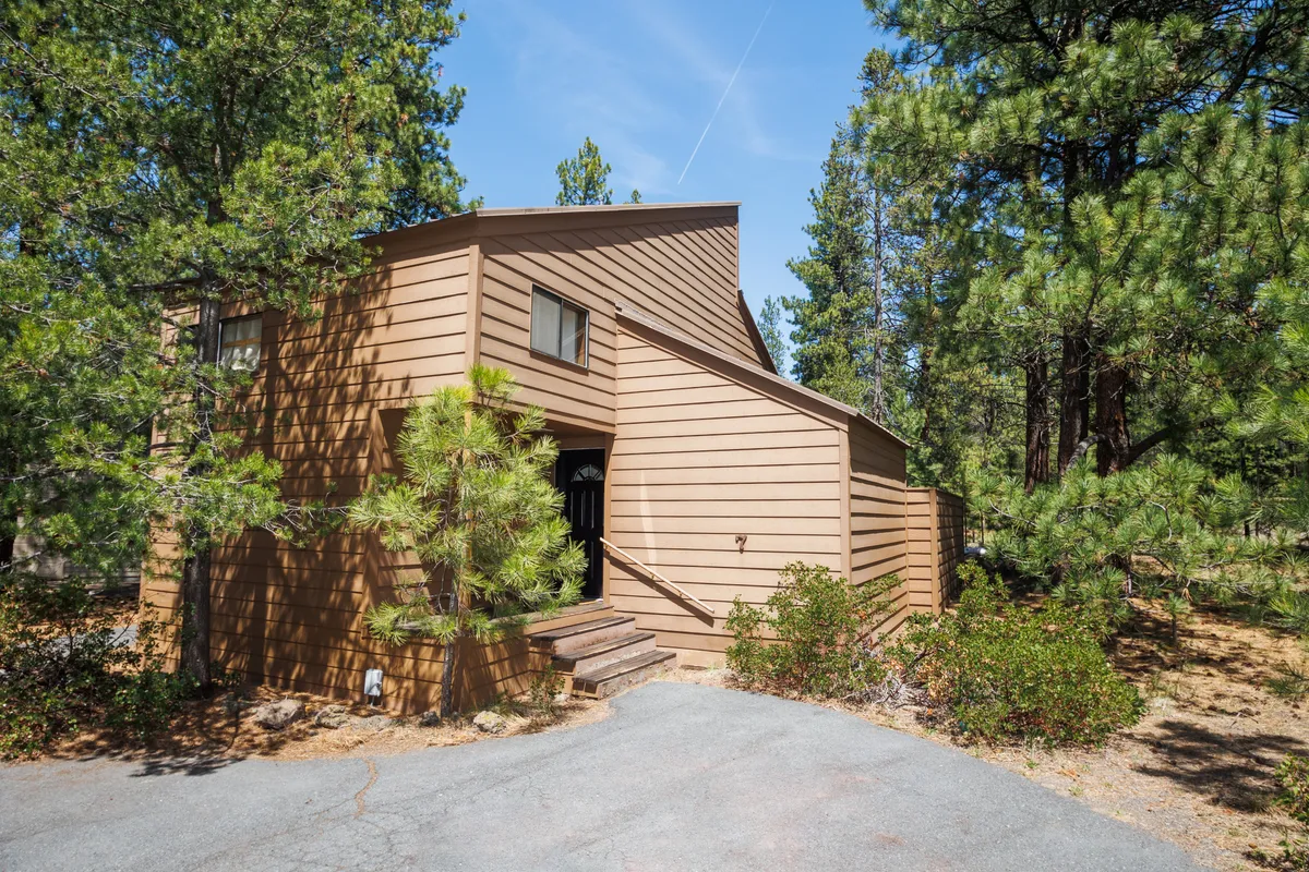 The image shows the inviting front entrance of the cabin, featuring warm wooden siding and nestled among towering trees. The serene outdoor surroundings highlight the peaceful environment and easy access to nature trails and family activities.