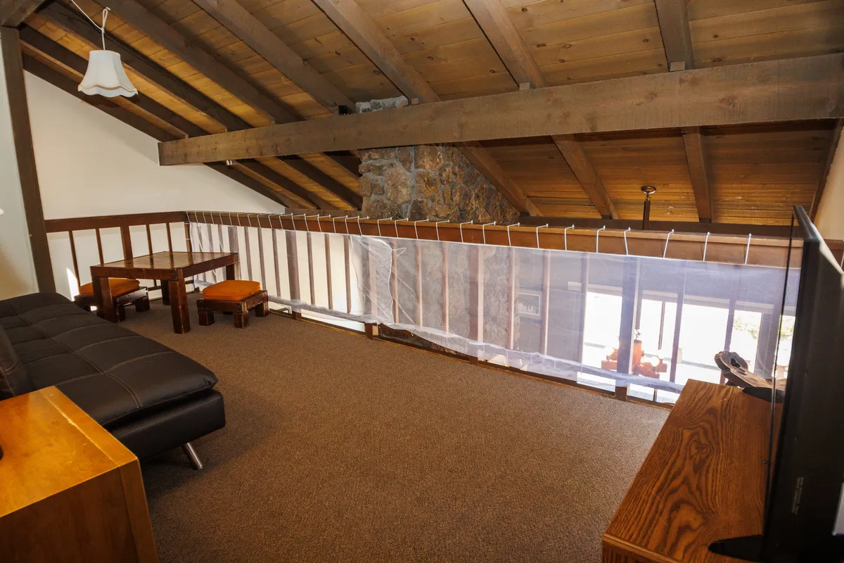 A comfortable loft space with wooden beams, a stone accent wall, a sofa, a wooden table, and a TV. The area is relaxed and versatile, suitable for movie nights, game sessions, or quiet reading—activities ideal for multi-generational groups.