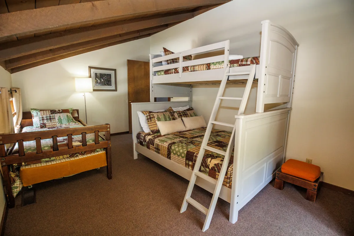 A playful bedroom scene with a bunk bed, single bed, warm lighting, and wooden furniture. The space feels inviting and is clearly designed with children or multiple guests in mind.