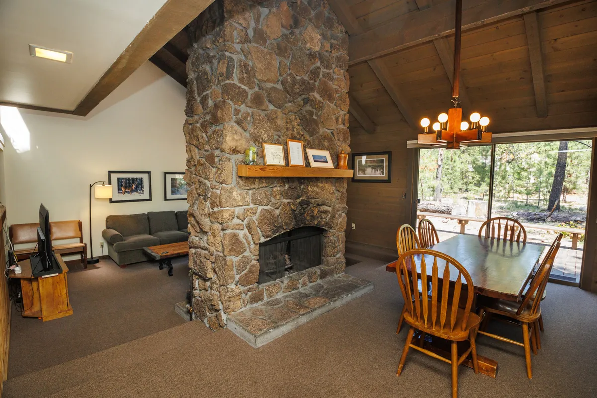 An inviting living and dining space with a central stone fireplace, a dining table set for family meals, plush sofas, and expansive windows that overlook the scenery outside. The space is designed for comfortable socializing, game nights, and memorable family dinners.