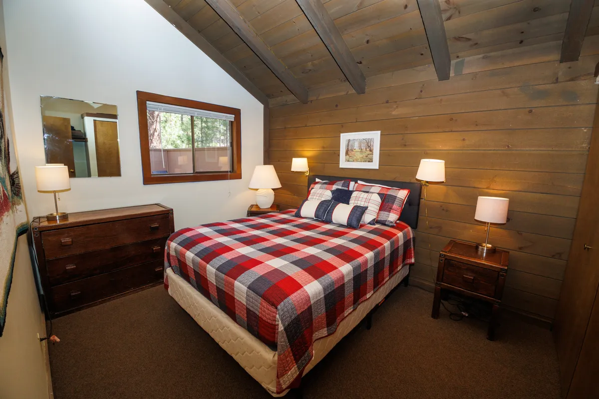 A welcoming bedroom scene with a bed dressed in plaid bedding, a wooden dresser, framed artwork, and soft lighting from bedside lamps. The room feels both warm and private, ideal for adults or grandparents seeking a restful retreat.